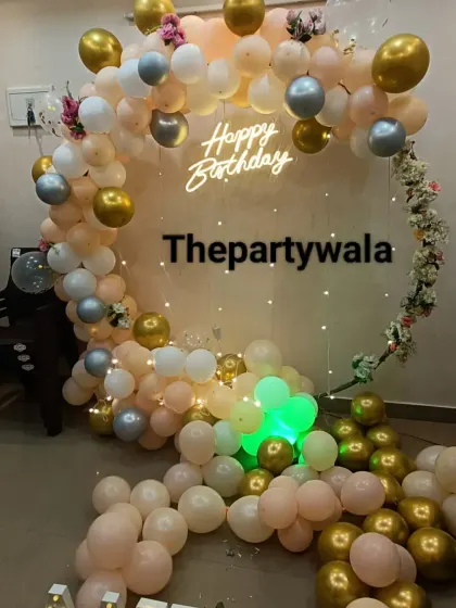 A cascade of peach, white, and gold balloons with a 'Happy Birthday' neon sign.
