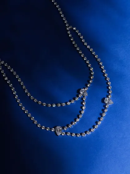A delicate, layered diamond necklace shot against a deep blue background. The simplicity of the setup allows the intricate details and sparkle of the piece to shine through.