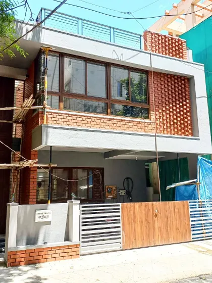 This is the exterior of a residence in Indiranagar, showcasing a blend of modern form with traditional materials. The facade features an intricate exposed brick jaali screen, which provides privacy and ventilation for the upper floor while creating a strong visual statement.