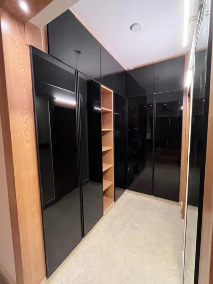 This walk-in closet combines natural wood tones with bold, black glass doors. The open shelving in the middle breaks up the dark surfaces and provides a beautiful spot for display, creating a highly functional and stylish dressing area.