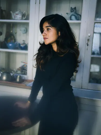 A portrait of a woman standing by a glass cabinet, bathed in soft, natural light. The motion blur on her hands adds a dynamic element to an otherwise still and contemplative moment.