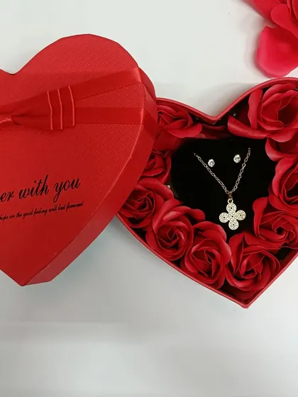 A closer look at the four-leaf clover necklace set, nestled among red roses. It's a symbol of good luck and love.