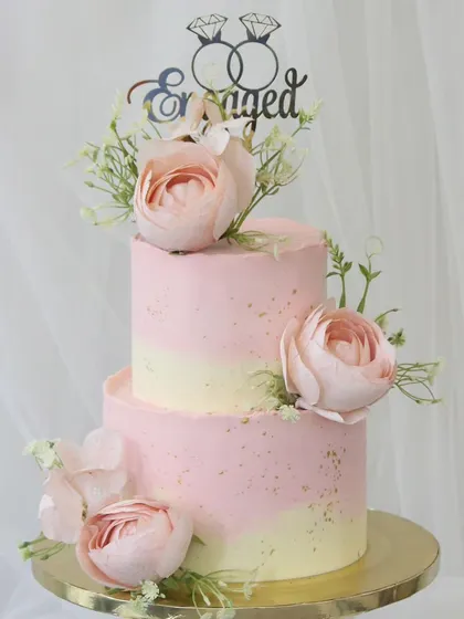 A lovely two-tiered engagement cake in soft shades of pink and cream. This piece is decorated with delicate sugar flowers and a custom "Engaged" topper, making it a perfect centerpiece for celebrating the special announcement.