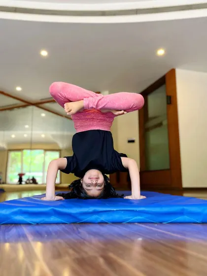 This young gymnast smiles while holding a challenging tucked headstand, showing her growing strength and confidence.