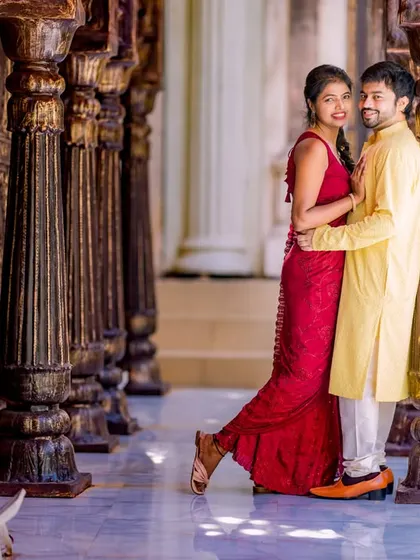 A romantic pose in a corridor of wooden pillars. The bride's red dress and the groom's yellow kurta create a beautiful, warm color palette.