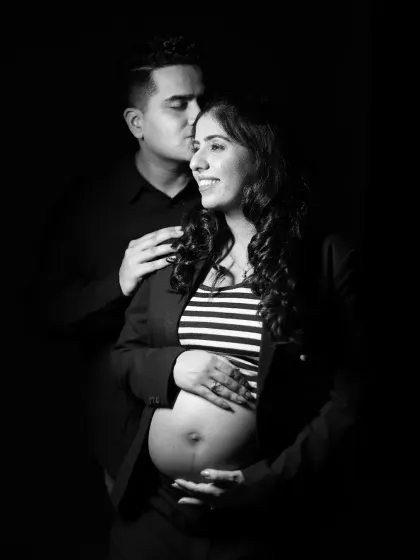 A dramatic low-key black and white portrait of a couple. The partner kisses the mother-to-be's head in this intimate and artistic shot.