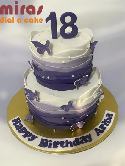 An elegant two-tier cake for an 18th birthday. The design features a purple ombre wave effect, accented with delicate purple butterflies and pearls for a sophisticated look.