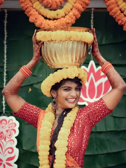 A happy bride poses with a decorated pot on her head during her Haldi ceremony, smiling for the camera.