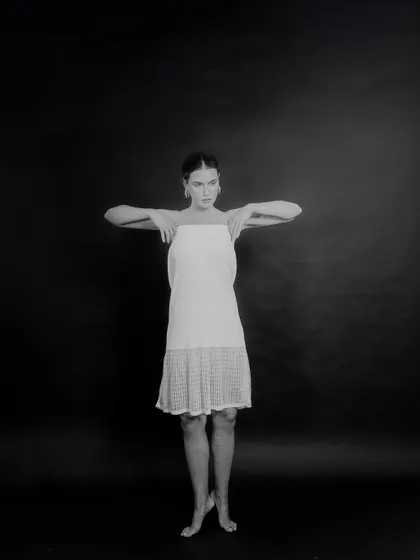 A black and white studio shot for Tululs against a dark background. The pose is inspired by dance, creating a sense of movement and grace within a minimalist setting.