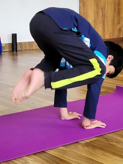 A young boy concentrates as he prepares to lift into crow pose. Building this kind of focus and strength is a key benefit of kids' yoga.