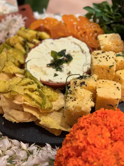 A traditional Indian snack platter featuring favorites like dhokla and crispy fried snacks, served with a creamy dip. This platter is a perfect addition to any festive gathering, offering familiar and beloved flavors.