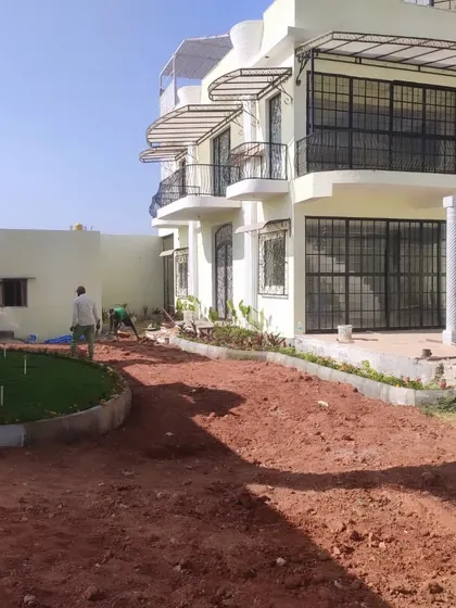 An early stage of a large residential landscaping project. The ground is prepared and graded, with the initial garden bed borders and a small patch of artificial turf already installed.