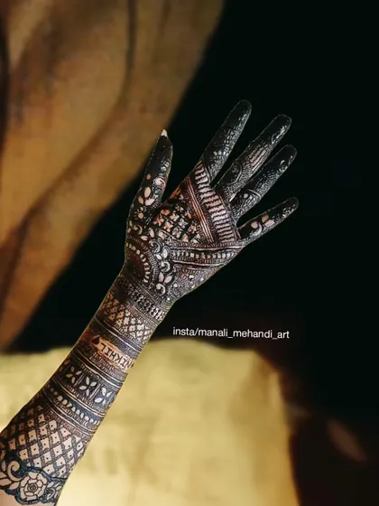 A beautiful example of an Arabic-style mehandi design on the back of the hand. The pattern uses bold lines, delicate shading, and negative space to create a flowing, elegant look.