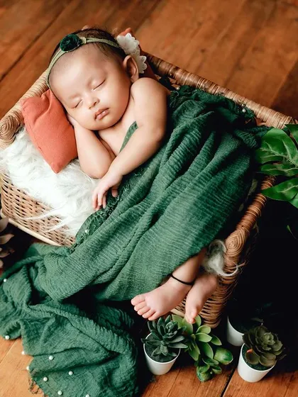 This high-angle shot shows the full setup, with the baby sleeping in a basket surrounded by potted plants for a natural, earthy vibe.
