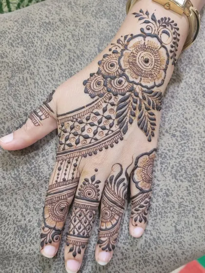 A close-up of a party henna design on the back of the hand, showing a beautiful floral cuff and intricate finger details.