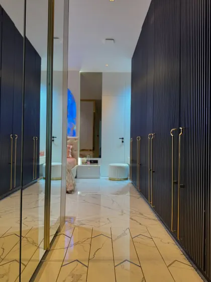 This walk-in closet, leading from the master bedroom, features deep blue fluted wardrobes with elegant gold handles. The full-length mirror at the end enhances the sense of space and reflects the beautiful bedroom beyond.