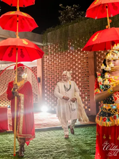 A royal groom entry, escorted by attendants with traditional red umbrellas, creating a regal and timeless visual.
