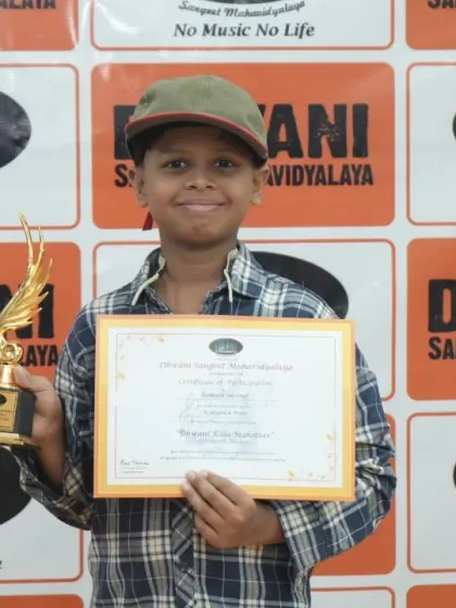 A young student in a cap smiles with his certificate and trophy.