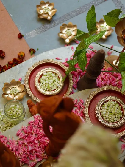 A top-down view of the decorative elements, including brass plates with jasmine and terracotta figurines on a bed of pink petals. The composition is rich in color and texture.