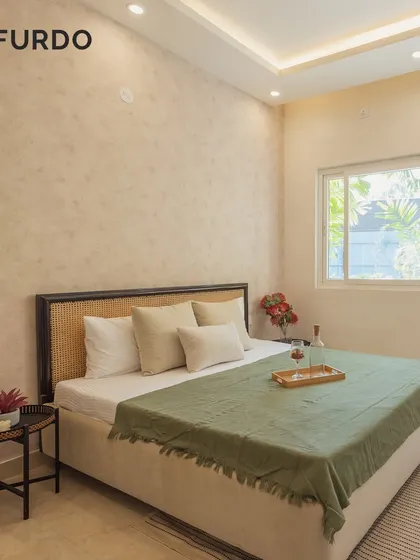 This bedroom showcases a minimalist aesthetic with a textured beige accent wall and a bed featuring a cane headboard. The large window allows for plenty of natural light, creating a bright and calming space.