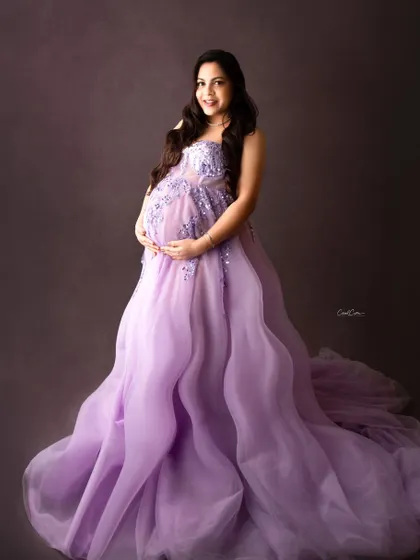 A classic, confident portrait. This mom-to-be cradles her bump in a beautiful lavender gown, radiating pure happiness.