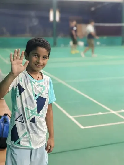 A happy young player waving from the court during our badminton match day. For us, the goal is always to make sports enjoyable.