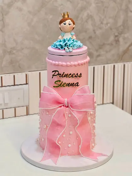 A tall, two-tier princess cake in pink, with a large bow and a princess figurine on top.