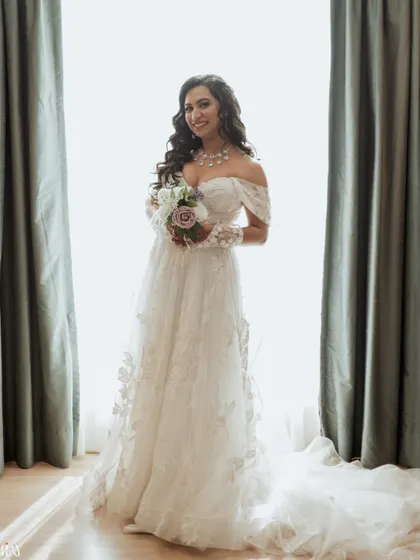 A beautiful bridal portrait, with the bride holding her bouquet and smiling, framed by soft window light.