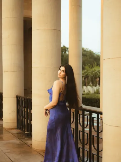 A wider shot from the same series, showing the wet ground and the grand pillars. The composition emphasizes the scale of the location and the elegance of the subject.