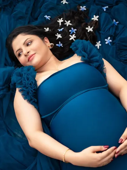 Lost in a dream. This overhead shot captures the mother-to-be lying on a bed of blue tulle, her expression peaceful and content. The small flowers scattered in her hair add a delicate, whimsical touch.