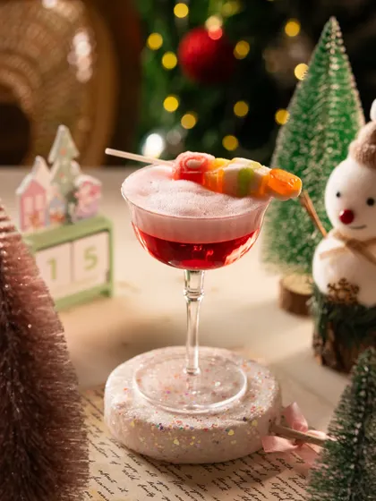A whimsical Christmas cocktail garnished with candy. The festive props like the snowman and calendar set the scene perfectly.