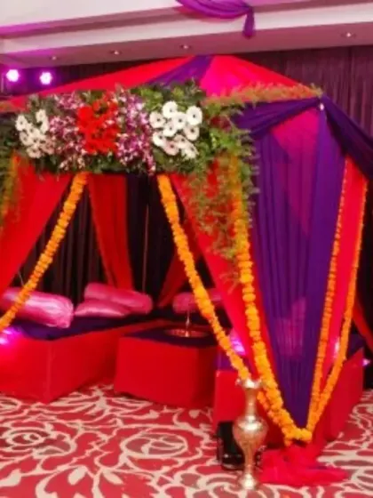 A decorative canopy tent for a traditional ceremony. This structure is draped in rich purple and red fabric with marigold garlands, creating a special enclosed space for rituals.
