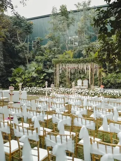A wide view of an outdoor ceremony, showing the elegant seating arrangement leading to a beautiful mandap set against a lush green backdrop.