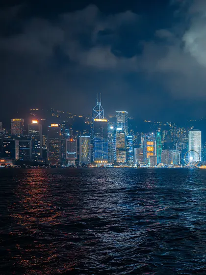 Another perspective of the Hong Kong skyline at night, capturing the vastness of the city and the sea. The moody clouds add a layer of drama to the scene.