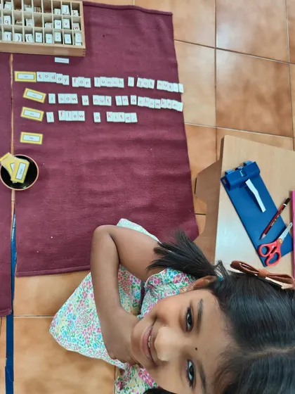 A proud smile from a child who has successfully used the Movable Alphabet to create sentences. This is the joy of "I did it myself!"