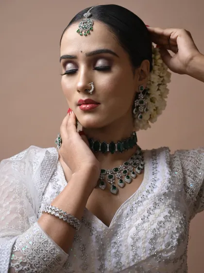 An elegant airbrush makeup look created as a demonstration for students, featuring a classic white saree with green jewelry. The skin finish is flawless.