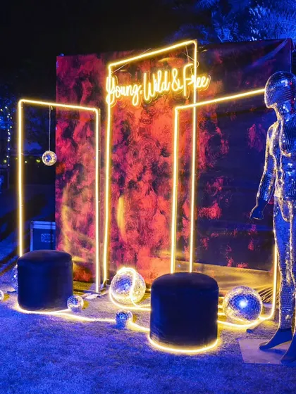A "Young, Wild & Free" photo booth. The neon sign, abstract backdrop, and disco ball mannequins created the perfect spot for fun, memorable pictures.