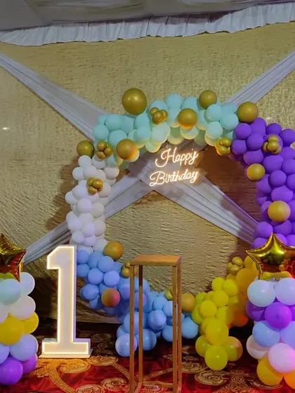 A colorful pastel balloon ring for a first birthday. This setup includes a light-up number '1', a neon sign, and star-topped balloon pillars.