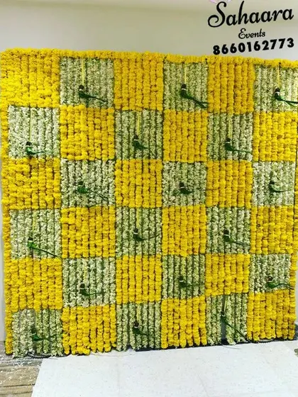 A cheerful baby shower backdrop with a checkerboard pattern of yellow and white flowers. The small green parrots add a playful and unique detail to the traditional floral design.