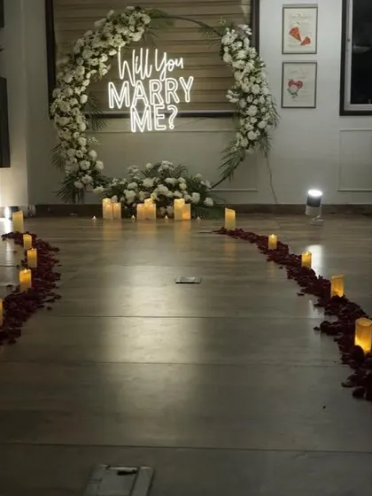 I create unforgettable romantic moments with setups like this surprise proposal. A candlelit path strewn with rose petals leads to a beautiful floral ring and a "Will You Marry Me?" neon sign, perfect for a terrace or indoor proposal.