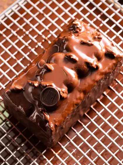 A rich, glossy chocolate loaf on a cooling rack. This behind-the-scenes style of shot gives a glimpse into the baking process and emphasizes freshness.