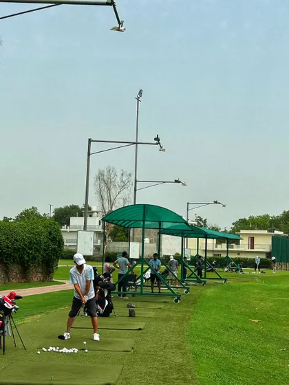 A golfer takes a practice swing at a covered bay, with the open range in front.