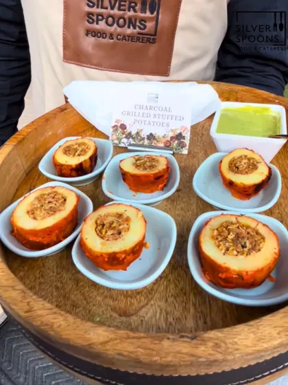 A server presents our Charcoal Grilled Stuffed Potatoes. These potatoes are hollowed out, filled with a savory stuffing, and grilled to perfection, served with a side of green chutney.