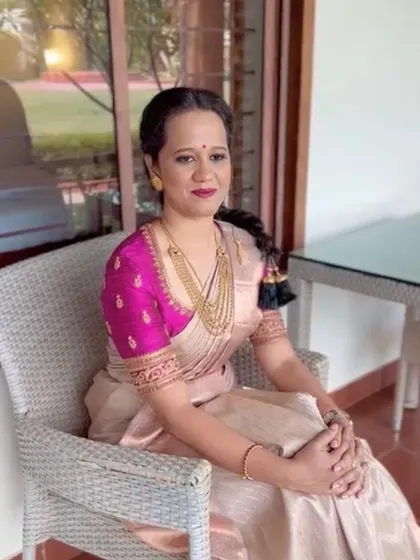 This client is styled in a beautiful beige Kanchipuram saree paired with a contrasting magenta raw silk blouse. The blouse features elegant hand embroidery, adding a pop of color and custom detail to her festive look.