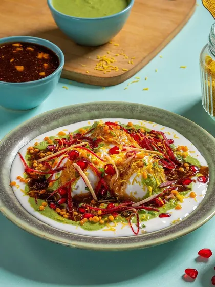 A plate of Dahi Bhalla, soft lentil dumplings soaked in creamy yogurt and topped with sweet and spicy chutneys and pomegranate seeds.