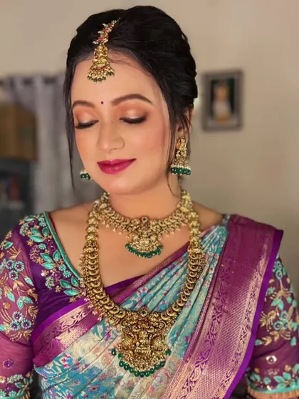 This bride from Mysore looks radiant in a unique peacock-toned silk saree. Her makeup features a soft pink and gold eye look with a matching lip color to complement her intricate floral blouse.