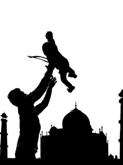 A creative black and white silhouette of a father lifting his child, perfectly framed against the iconic outline of the Taj Mahal.
