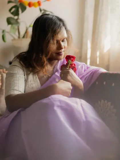 A tender moment captured indoors by a window. The model holds red roses, her expression soft and contemplative, as natural light fills the scene.