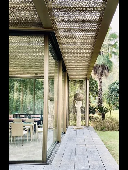 A side view of the glass pavilion, showing its slender steel frame and the seamless transition to the surrounding lawn. The design is an exercise in structural minimalism.