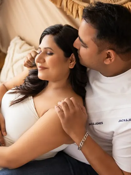 An intimate moment in the same boho setting. The partner gently kisses the mom-to-be's cheek as she closes her eyes, creating a peaceful and loving portrait.
